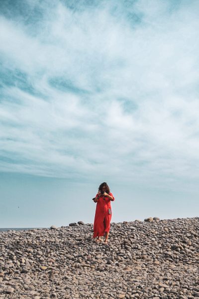 curso de mirada fotografía en alicante mujer con vestido rojo haciendo una foto en una playa de piedra